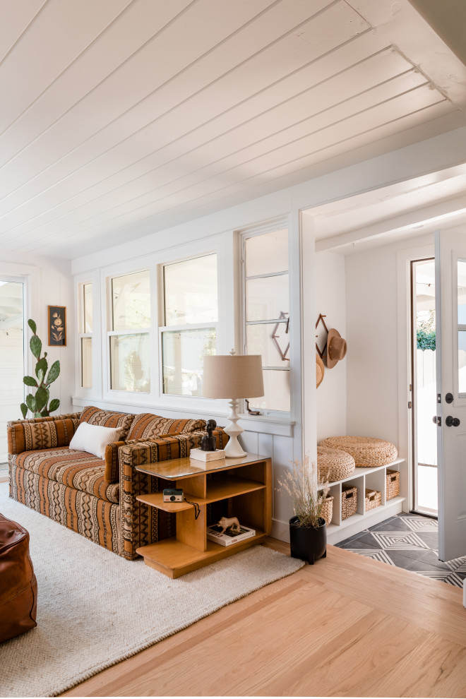 Diseño de sala de estar abierta costera con paredes blancas, suelo de madera clara y suelo beige