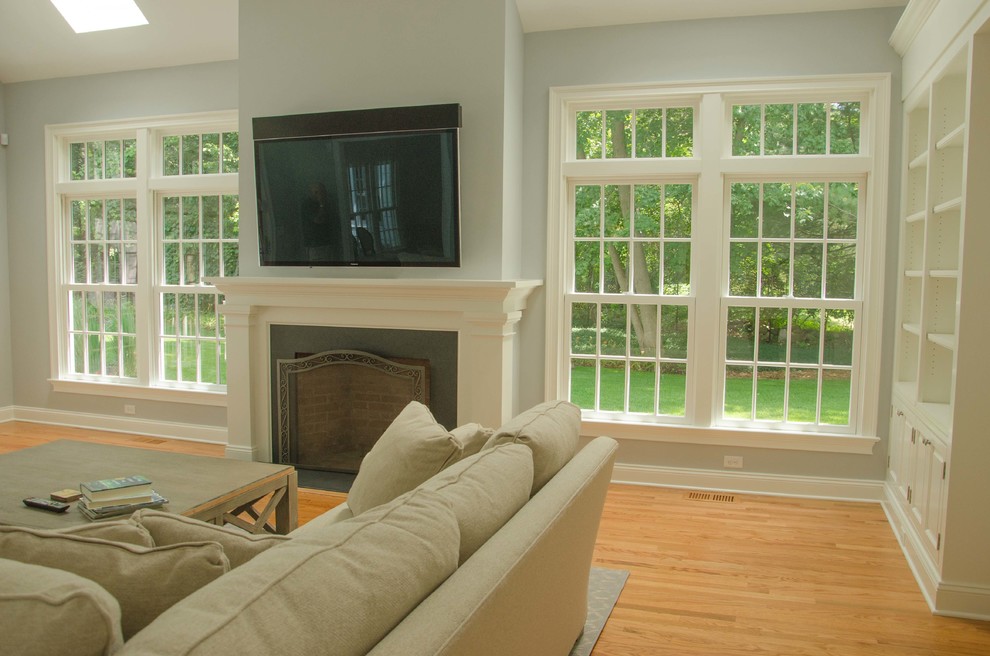 Imagen de sala de estar tradicional de tamaño medio con paredes azules, suelo de madera clara, todas las chimeneas, marco de chimenea de piedra y pared multimedia