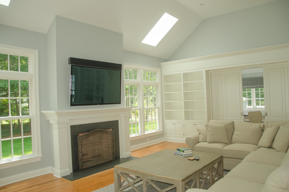 Large elegant enclosed light wood floor and brown floor family room photo in New York with blue walls, a standard fireplace, a wall-mounted tv and a wood fireplace surround