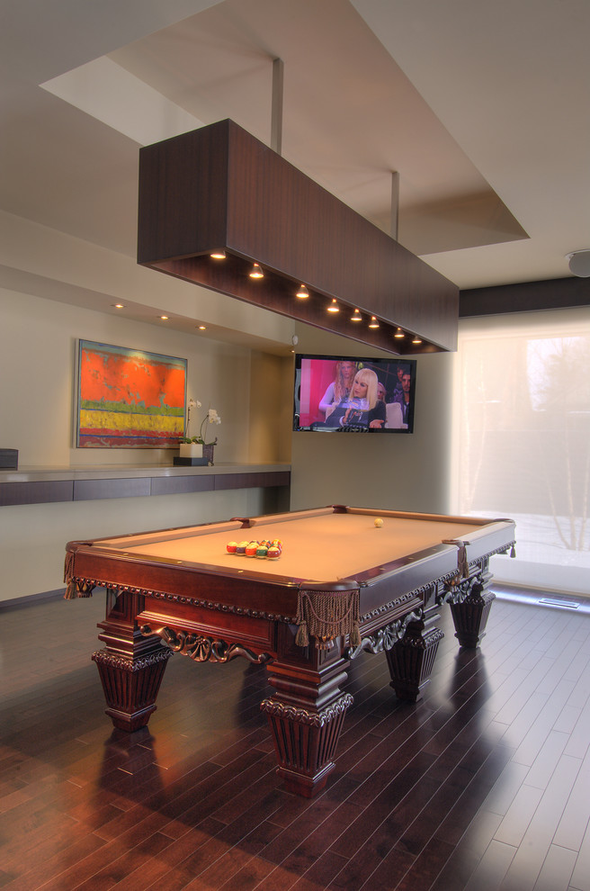 Modelo de sala de estar actual de tamaño medio con paredes beige, suelo de madera oscura, televisor colgado en la pared y suelo marrón