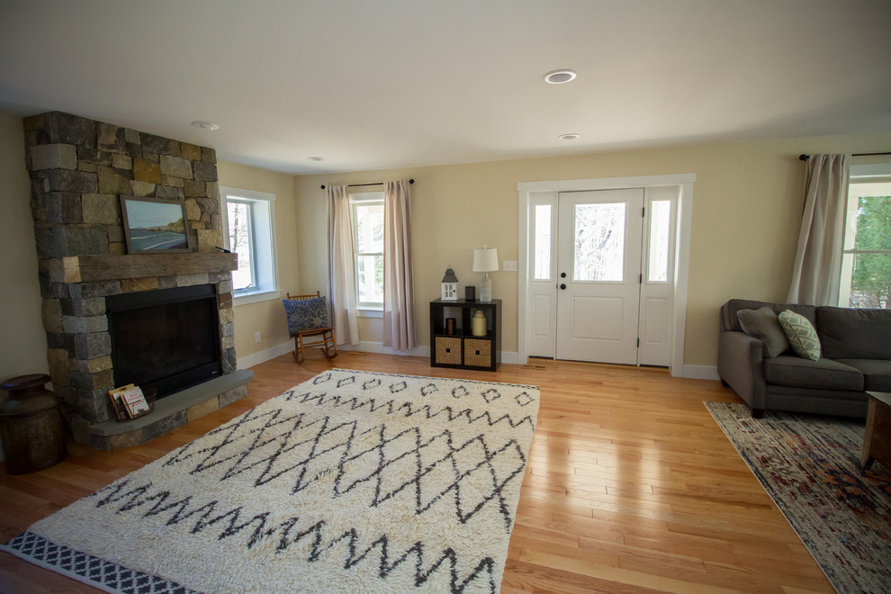 Mittelgroßes Country Wohnzimmer mit beiger Wandfarbe, hellem Holzboden, Kamin, Kaminumrandung aus Stein, freistehendem TV und braunem Boden in New York