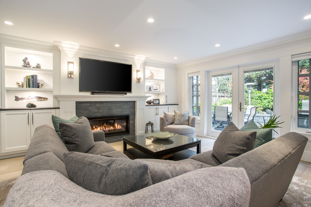 Mittelgroßes, Offenes Klassisches Wohnzimmer mit weißer Wandfarbe, braunem Holzboden, Kamin, Kaminumrandung aus Stein, TV-Wand und grauem Boden in Vancouver