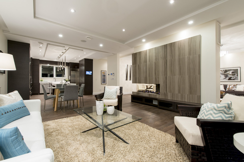 Imagen de sala de estar abierta moderna grande con suelo de madera en tonos medios, chimenea de doble cara y marco de chimenea de madera