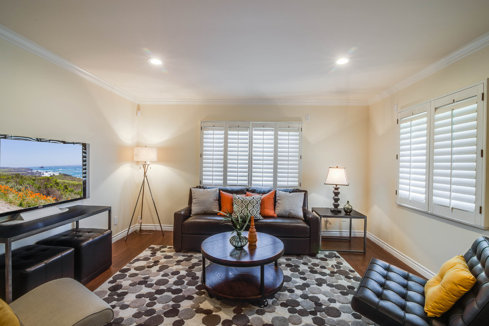 Kleines, Offenes Klassisches Wohnzimmer mit gelber Wandfarbe, braunem Holzboden, Kamin, Kaminumrandung aus Stein und freistehendem TV in Los Angeles