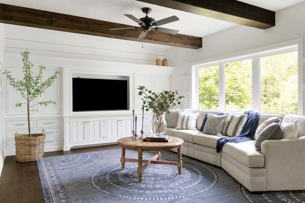 Cette image montre une grande salle de séjour traditionnelle ouverte avec un mur blanc, parquet foncé, un sol marron et un téléviseur encastré.