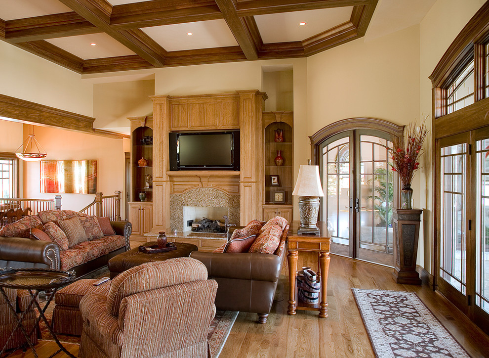 Ejemplo de sala de estar abierta de estilo de casa de campo grande con paredes beige, suelo de madera clara, todas las chimeneas, marco de chimenea de piedra y televisor colgado en la pared