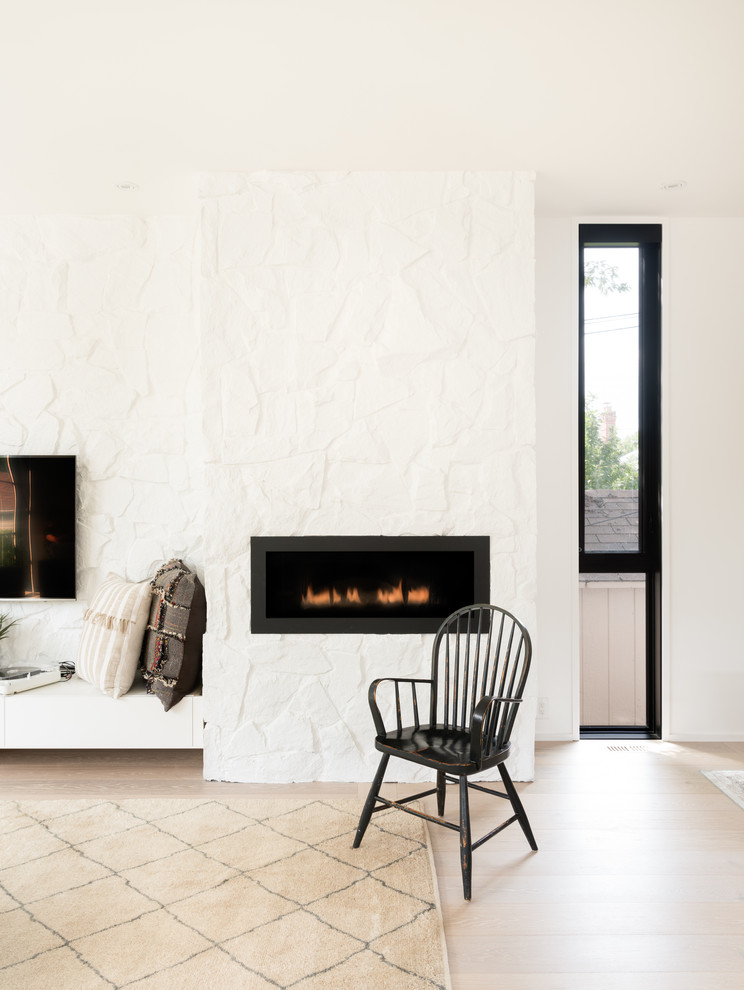 Modelo de sala de estar abierta escandinava con paredes blancas, suelo de madera clara, chimenea lineal, marco de chimenea de piedra, televisor colgado en la pared y suelo blanco