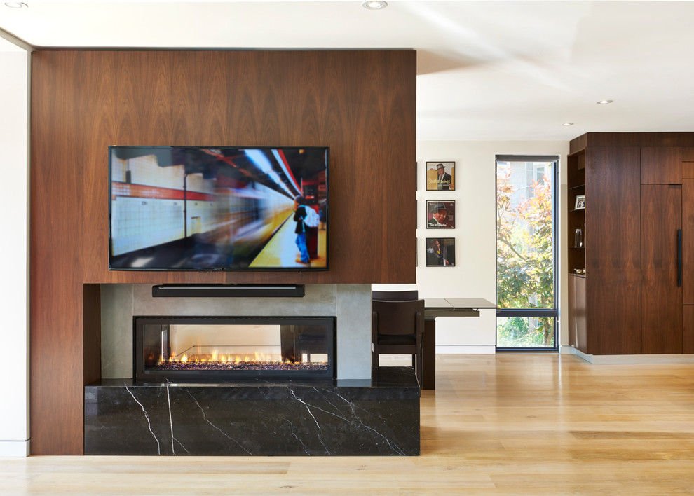 Modelo de sala de estar abierta contemporánea de tamaño medio con paredes blancas, suelo de madera clara, chimenea de doble cara, marco de chimenea de hormigón y pared multimedia