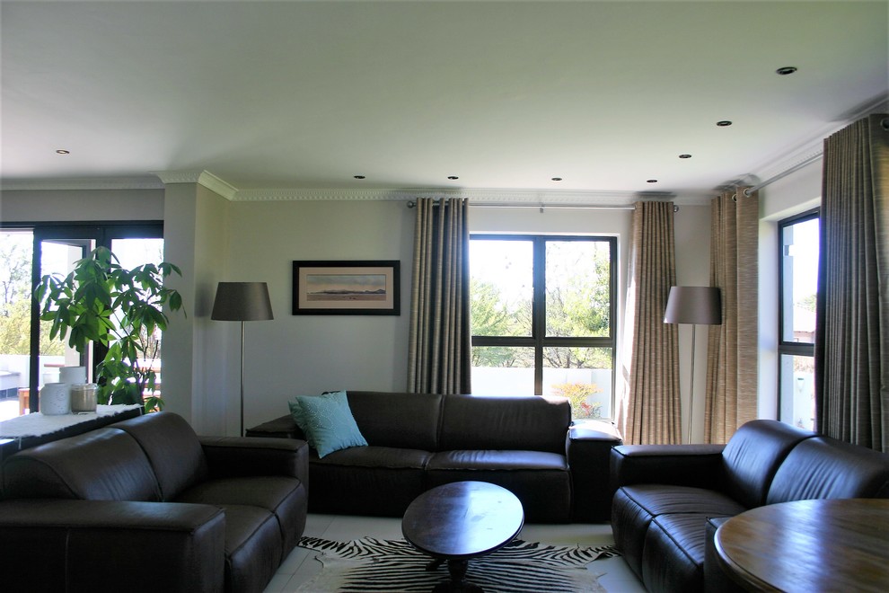Immagine di un grande soggiorno minimalista aperto con angolo bar, pareti beige, pavimento in gres porcellanato, TV a parete e pavimento bianco