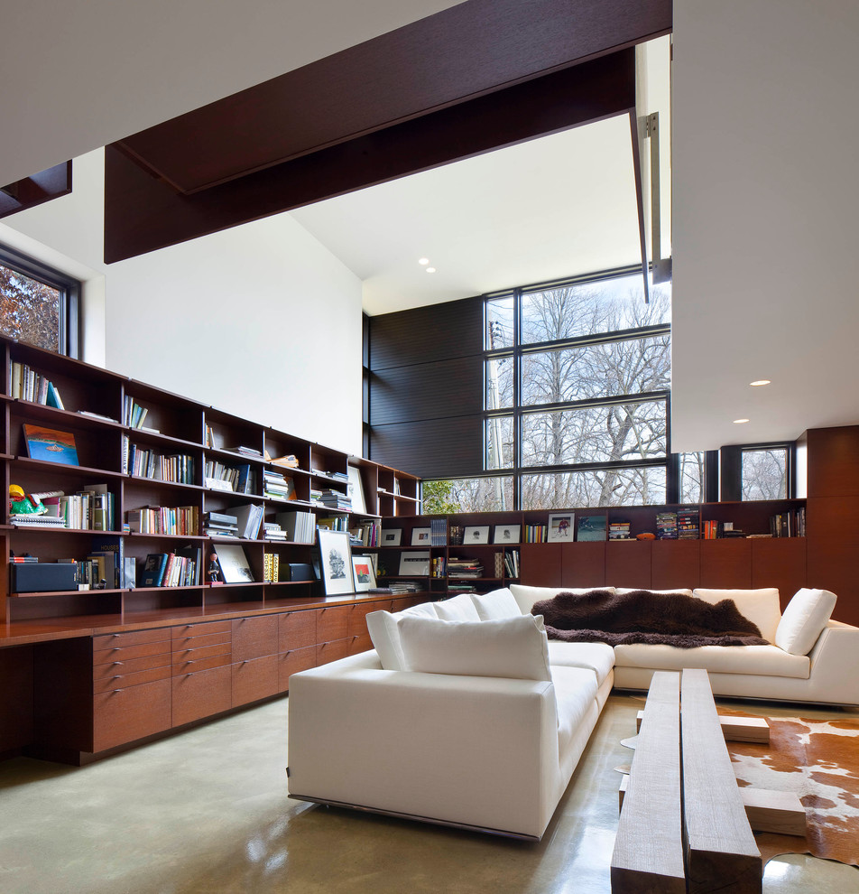 На фото: большая открытая гостиная комната в стиле модернизм с белыми стенами, бетонным полом и с книжными шкафами и полками