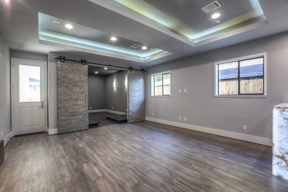 Großer, Abgetrennter Moderner Hobbyraum mit grauer Wandfarbe, dunklem Holzboden, Tunnelkamin, Kaminumrandung aus Stein, TV-Wand und grauem Boden in Houston