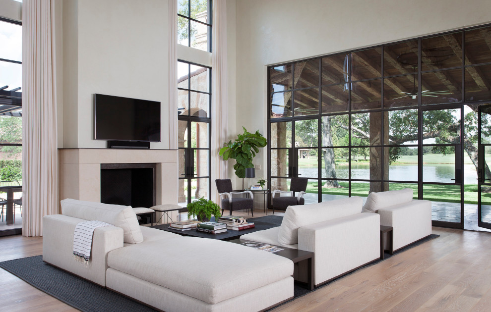 Modelo de sala de estar abierta mediterránea con suelo de madera clara, todas las chimeneas, televisor colgado en la pared y paredes blancas