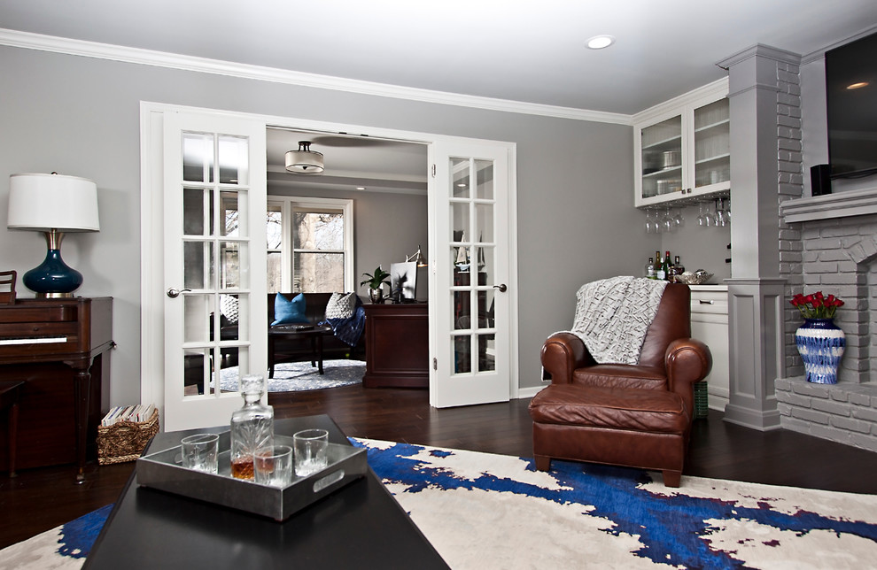 На фото: открытая гостиная комната среднего размера в стиле неоклассика (современная классика) с серыми стенами, темным паркетным полом, стандартным камином, фасадом камина из кирпича и телевизором на стене с