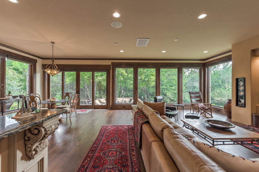 Imagen de sala de estar abierta de estilo americano de tamaño medio sin chimenea con paredes beige, suelo de madera oscura, televisor colgado en la pared y suelo marrón