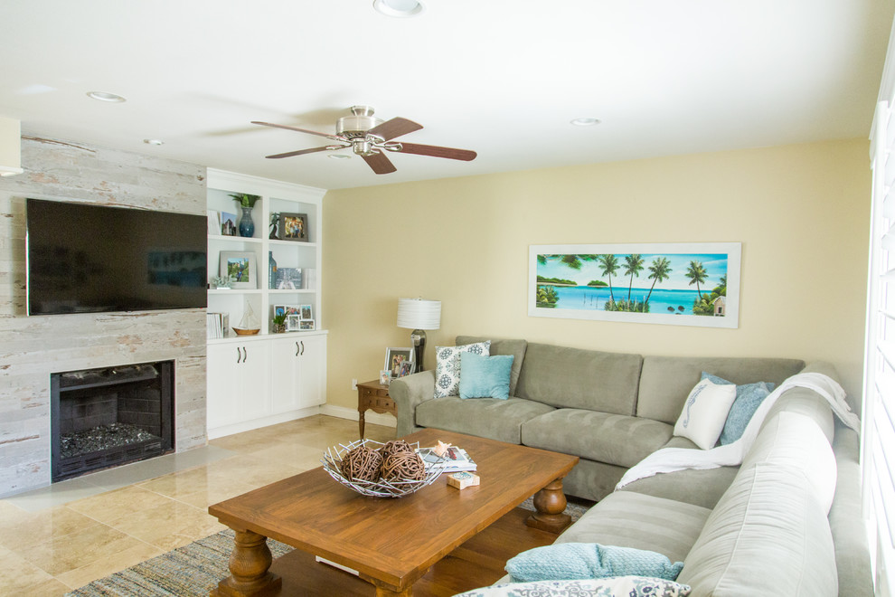 Medium sized beach style open plan games room in Orange County with beige walls, travertine flooring, a standard fireplace, a wall mounted tv, beige floors and a wooden fireplace surround.