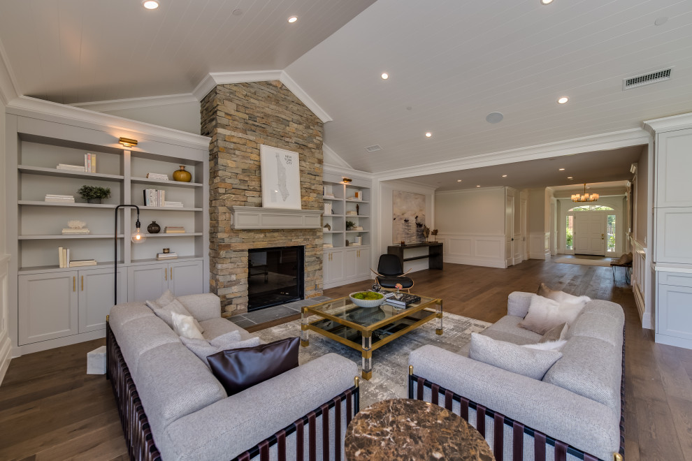 Photo of a large traditional open plan games room in Los Angeles with white walls, medium hardwood flooring, a standard fireplace, a stone fireplace surround, a concealed tv, brown floors, a vaulted ceiling and panelled walls.