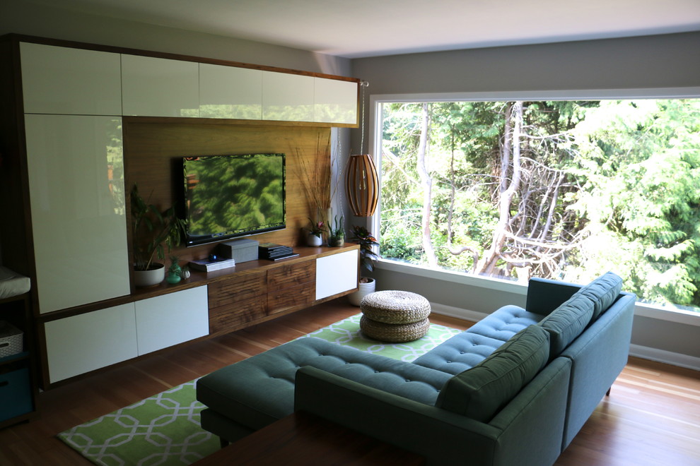 Imagen de sala de estar abierta actual de tamaño medio con paredes grises, suelo de madera en tonos medios y televisor colgado en la pared