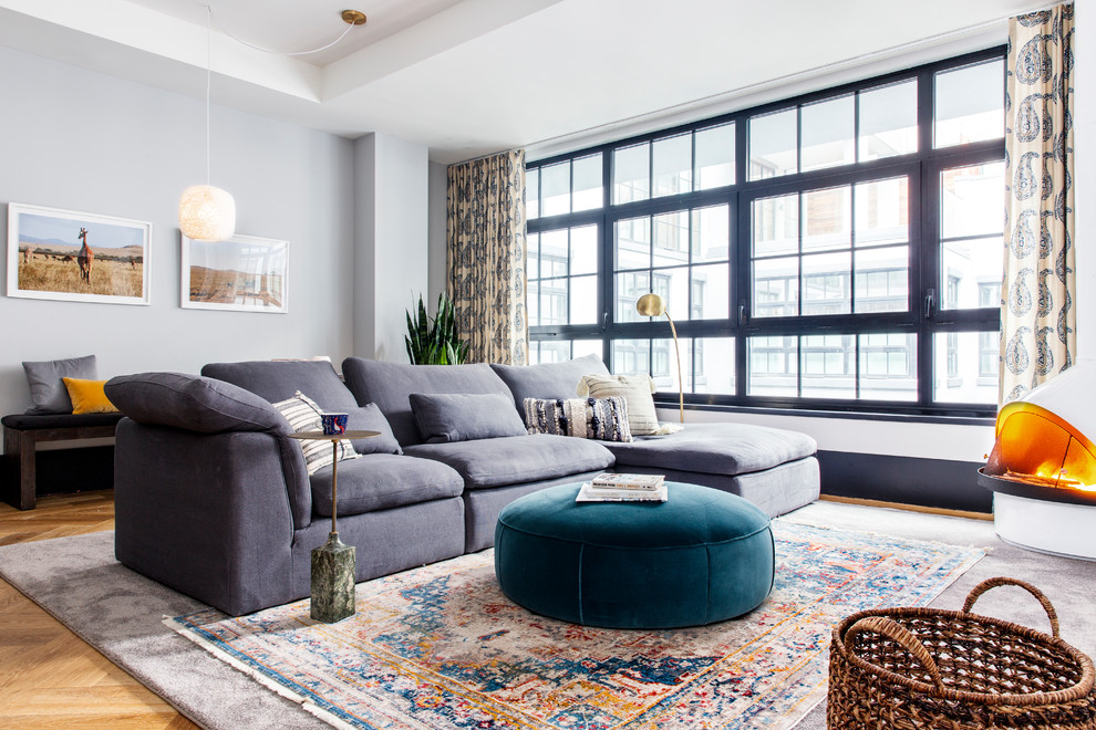 Modelo de sala de estar abierta ecléctica con paredes grises, suelo de madera en tonos medios y estufa de leña