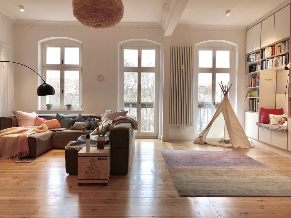 Diseño de sala de estar abierta actual de tamaño medio con paredes blancas, suelo de madera clara, estufa de leña, marco de chimenea de yeso y suelo marrón