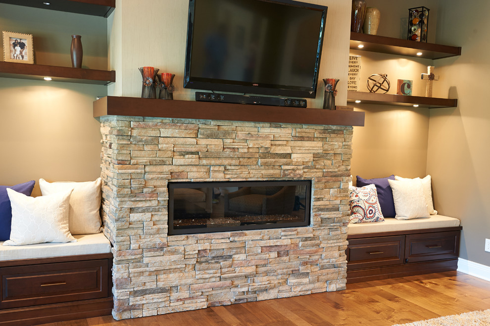 Modelo de sala de estar abierta clásica con paredes beige, suelo de madera en tonos medios, chimenea lineal, marco de chimenea de piedra y televisor colgado en la pared