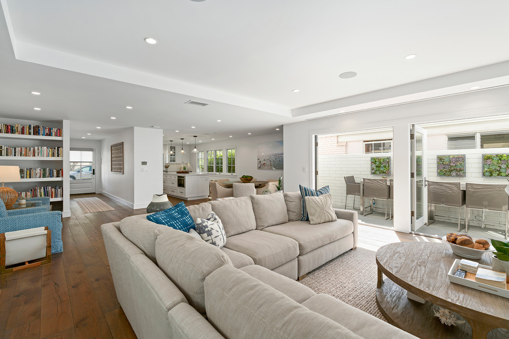 Modelo de sala de estar abierta clásica renovada grande con paredes blancas, suelo de madera en tonos medios y televisor colgado en la pared