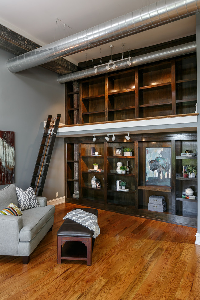 Cette image montre une salle de séjour mansardée ou avec mezzanine urbaine avec une bibliothèque ou un coin lecture, un mur gris et un sol en bois brun.