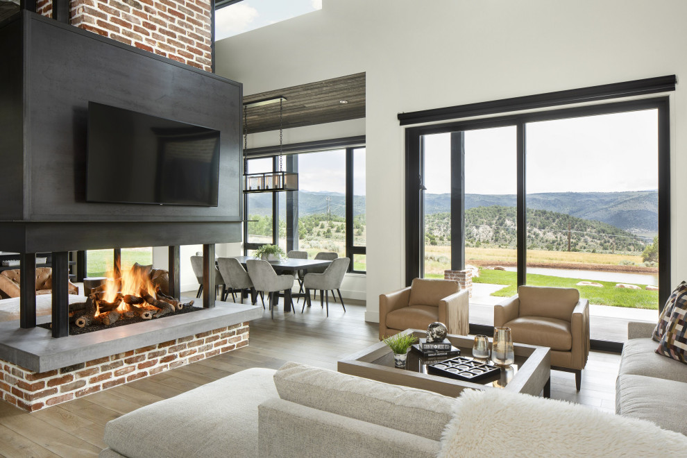 Example of an urban open concept light wood floor, brown floor, vaulted ceiling and brick wall family room design in Denver with a bar, white walls, a two-sided fireplace, a brick fireplace and a wall-mounted tv