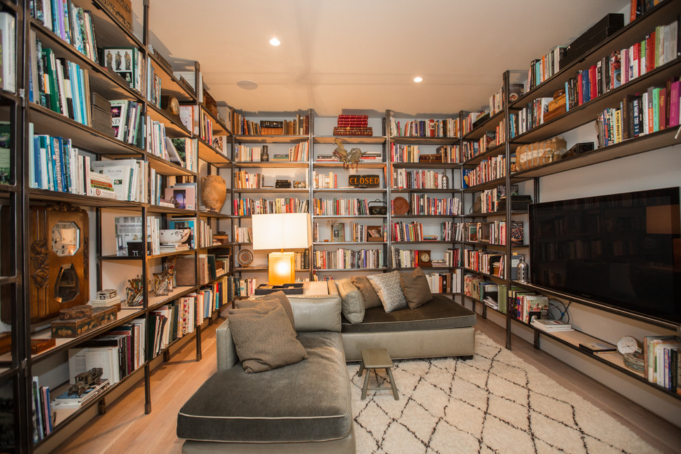 Modelo de sala de estar con biblioteca clásica renovada con paredes blancas, suelo de madera clara, televisor colgado en la pared y suelo beige