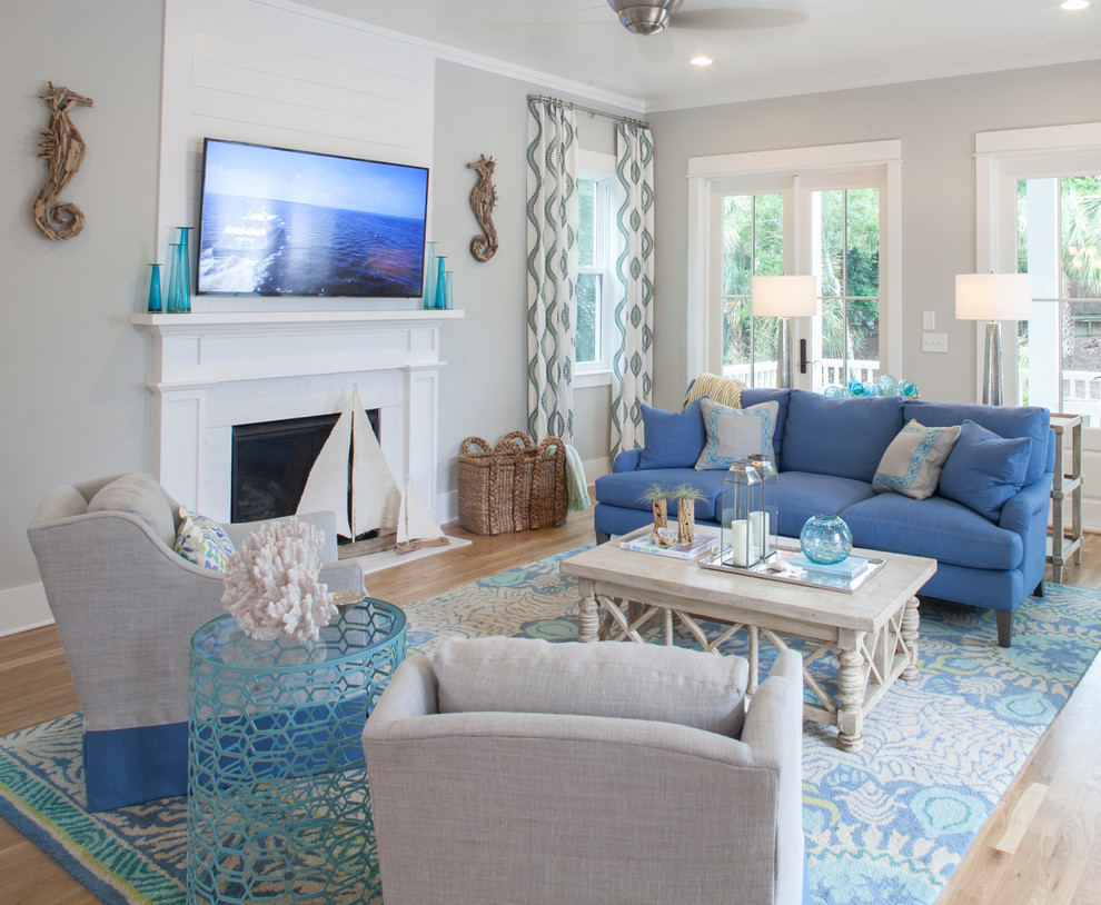 ローリーにあるビーチスタイルのおしゃれなオープンリビング (グレーの壁、淡色無垢フローリング、標準型暖炉、壁掛け型テレビ、青いソファ) の写真
