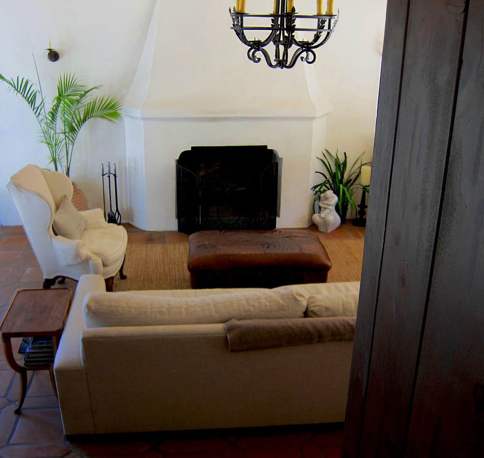 サンタバーバラにある高級な中くらいな地中海スタイルのおしゃれな独立型ファミリールーム (白い壁、テラコッタタイルの床、標準型暖炉、コンクリートの暖炉まわり、赤い床) の写真