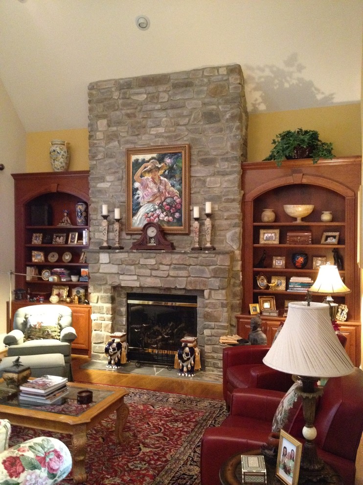 Imagen de sala de estar con biblioteca abierta rural de tamaño medio con paredes amarillas, suelo de madera clara, todas las chimeneas y marco de chimenea de piedra