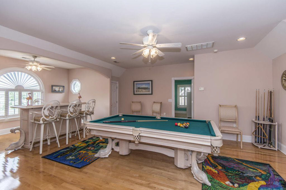 Design ideas for a large world-inspired enclosed games room in Orlando with a home bar, pink walls, light hardwood flooring, a corner fireplace, a wooden fireplace surround, a freestanding tv and brown floors.