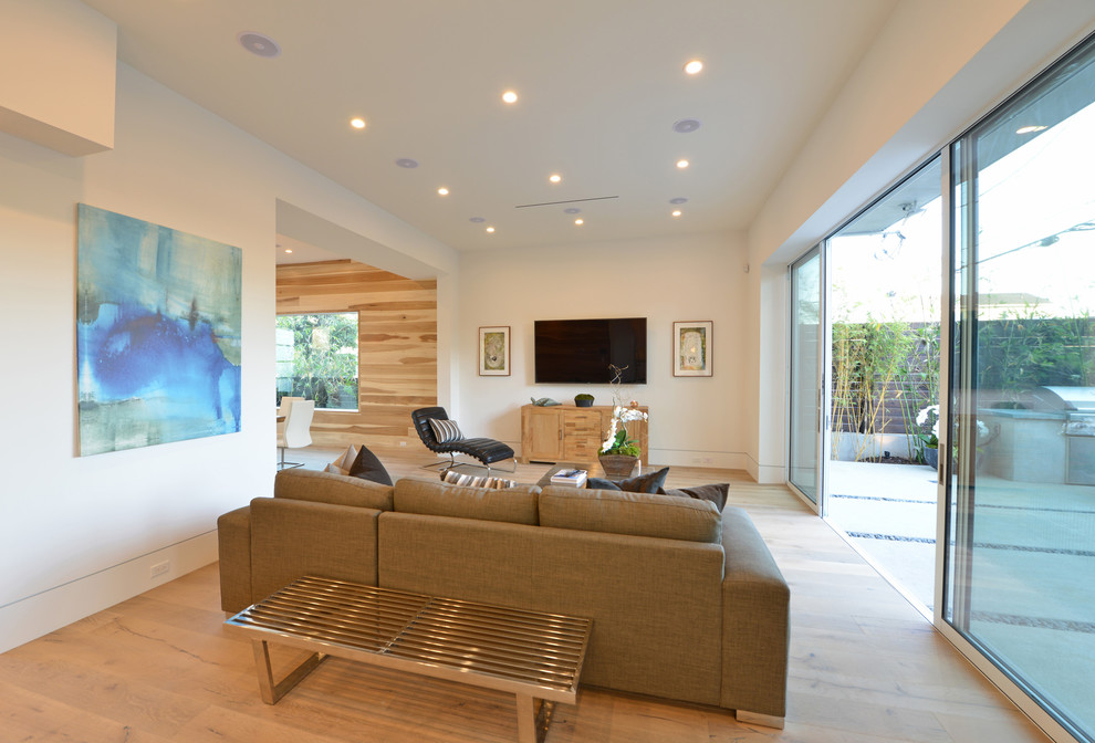 Exempel på ett mellanstort modernt allrum med öppen planlösning, med vita väggar, ljust trägolv, en väggmonterad TV och beiget golv
