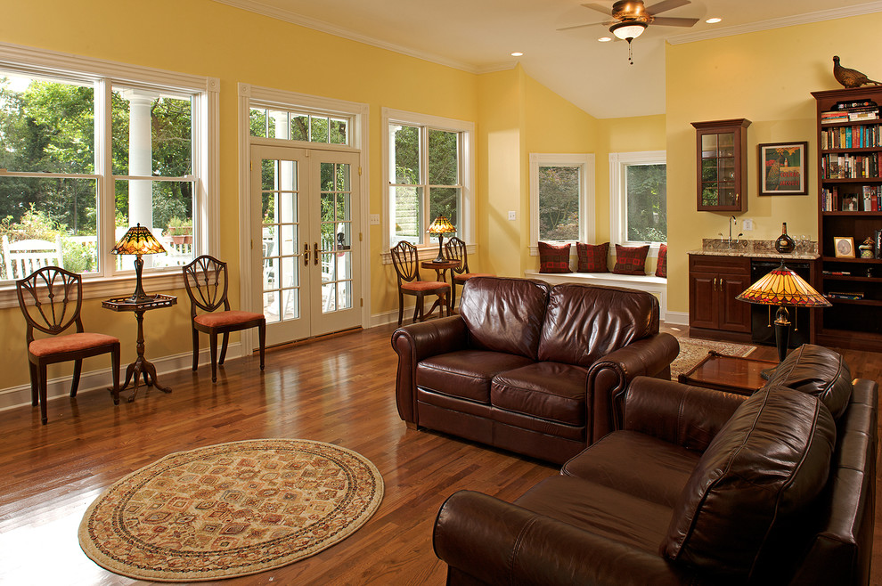 Diseño de sala de estar con biblioteca cerrada tradicional grande con paredes amarillas, suelo de madera clara y televisor colgado en la pared