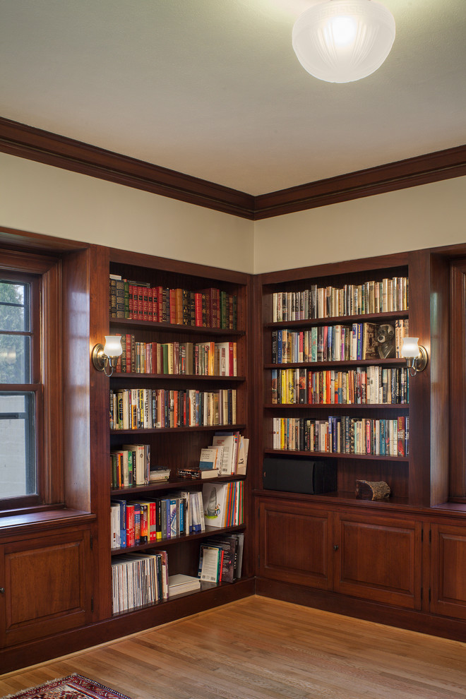 Cette photo montre une salle de séjour craftsman de taille moyenne avec une bibliothèque ou un coin lecture, un mur beige, parquet clair et un téléviseur encastré.