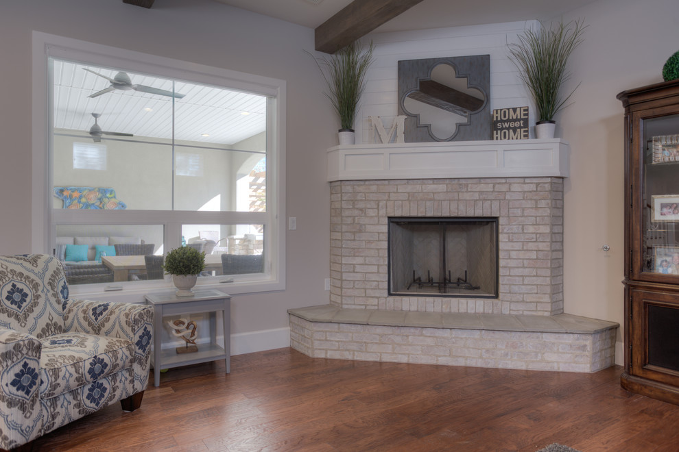 This is an example of a medium sized classic open plan games room in Albuquerque with beige walls, dark hardwood flooring, a corner fireplace, a brick fireplace surround and a built-in media unit.