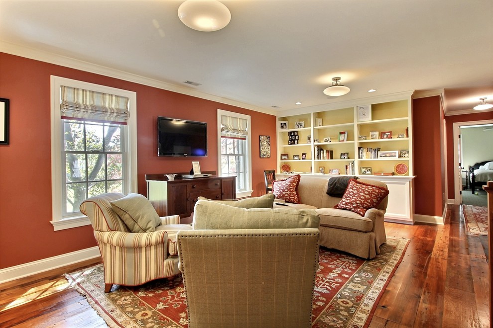 Пример оригинального дизайна: гостиная комната в классическом стиле с оранжевыми стенами, паркетным полом среднего тона и телевизором на стене