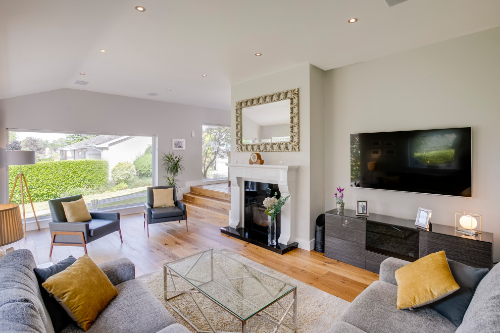 Mittelgroßes, Offenes Modernes Wohnzimmer mit weißer Wandfarbe, braunem Holzboden, Kamin, Kaminumrandung aus Stein und TV-Wand in Dublin