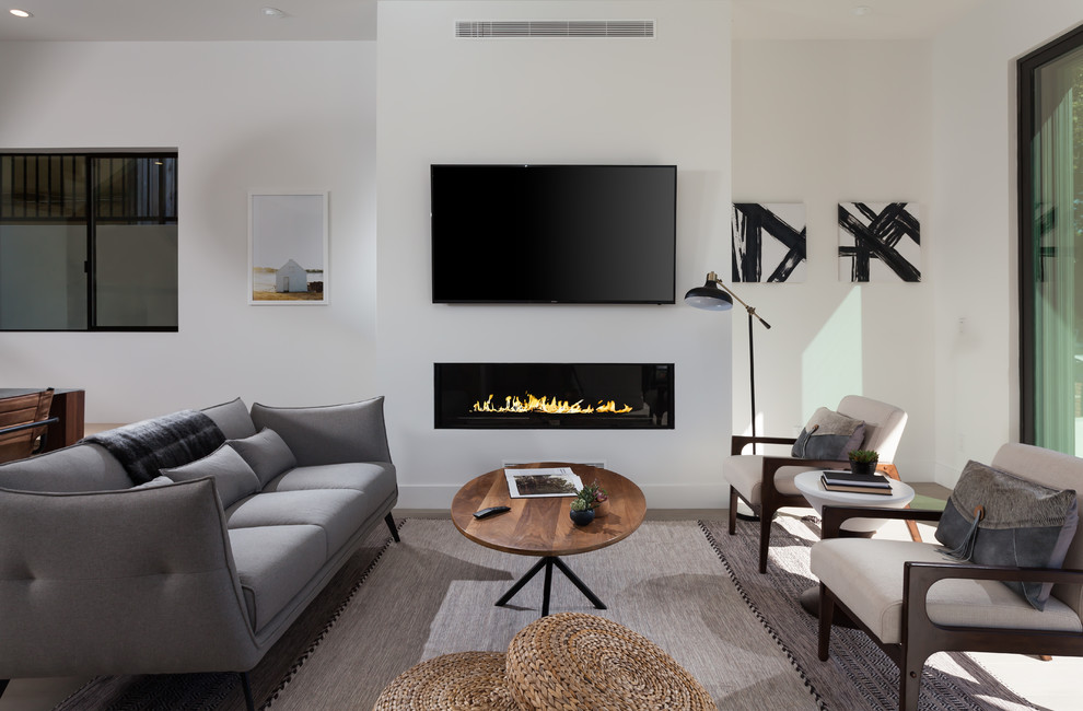 Стильный дизайн: открытая гостиная комната в современном стиле с белыми стенами, горизонтальным камином, телевизором на стене и ковром на полу - последний тренд