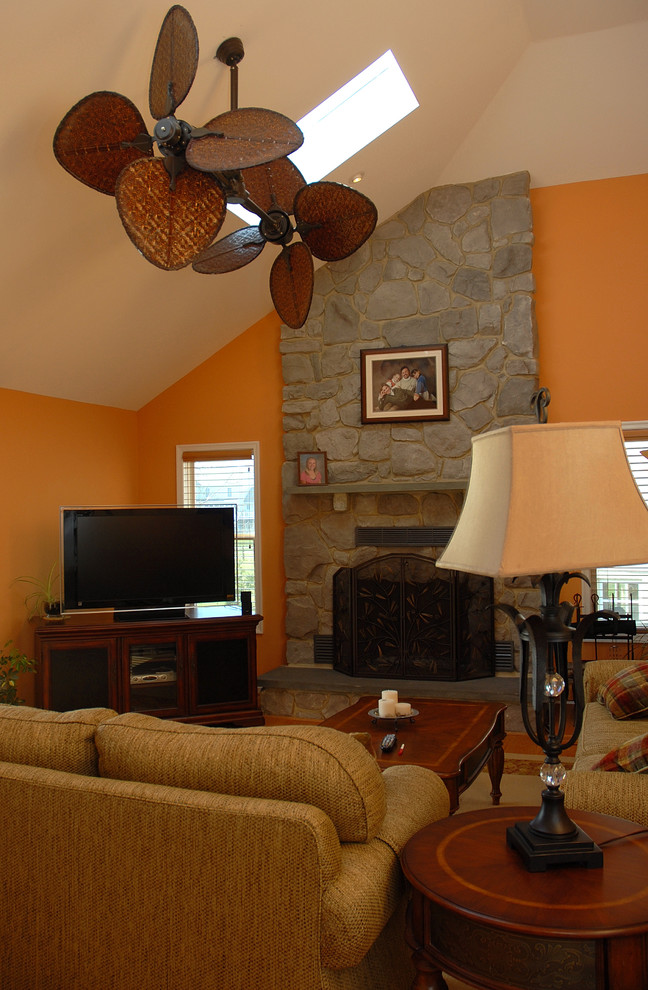 На фото: гостиная комната в стиле рустика с оранжевыми стенами, стандартным камином, фасадом камина из камня и телевизором в углу