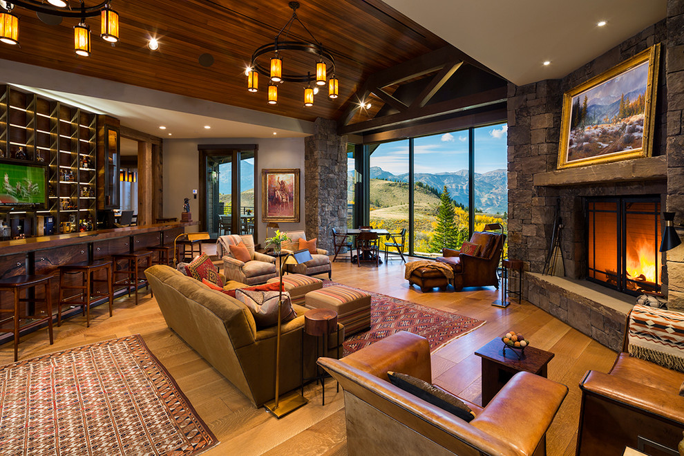 Large rustic open plan games room in Other with medium hardwood flooring, a stone fireplace surround, a standard fireplace, beige walls, no tv and brown floors.