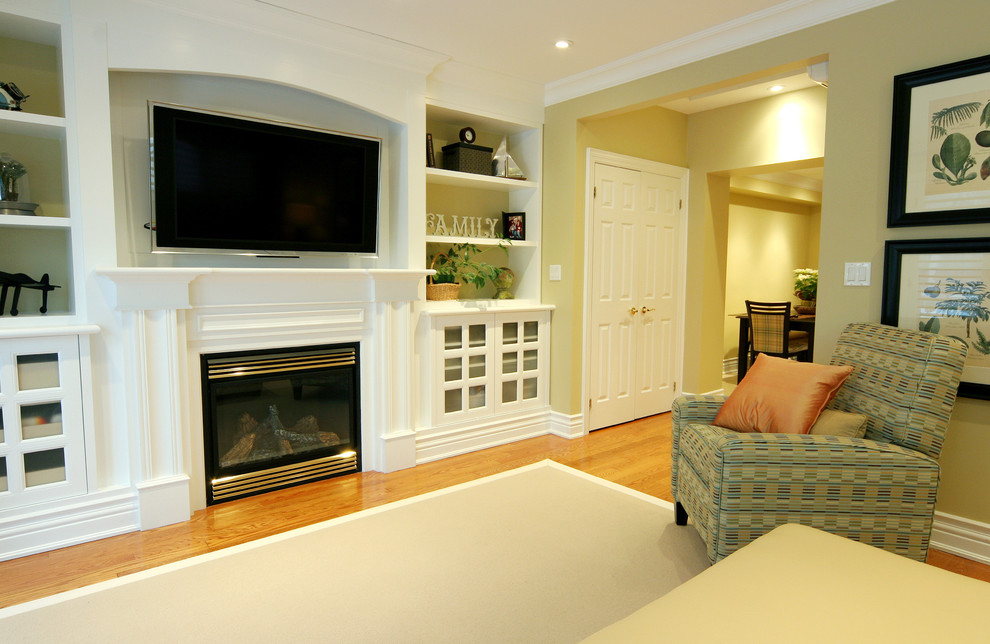 Photo of a medium sized classic enclosed games room in Toronto with a standard fireplace, a wooden fireplace surround, a wall mounted tv, yellow walls and light hardwood flooring.