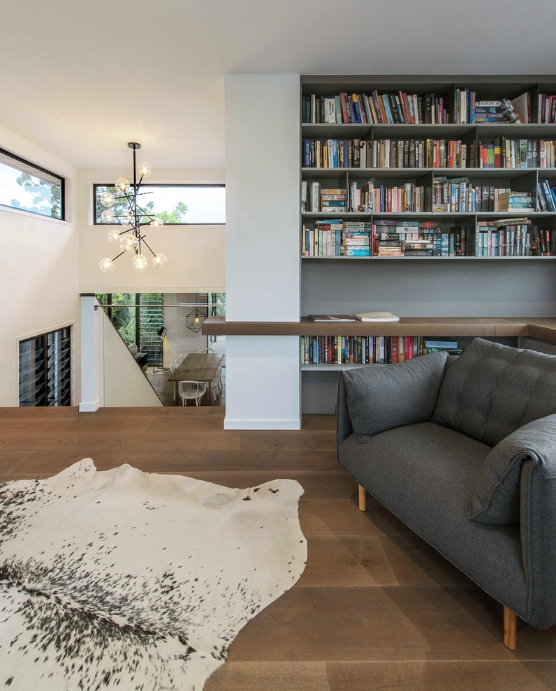 Idée de décoration pour une salle de séjour mansardée ou avec mezzanine design avec une bibliothèque ou un coin lecture, un mur blanc, un sol en bois brun et un sol marron.