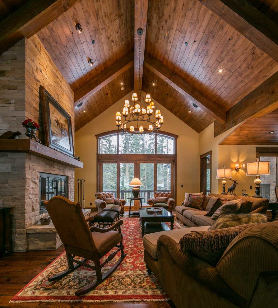 Imagen de sala de estar abierta rural grande sin televisor con paredes beige, suelo de madera en tonos medios, todas las chimeneas y marco de chimenea de piedra