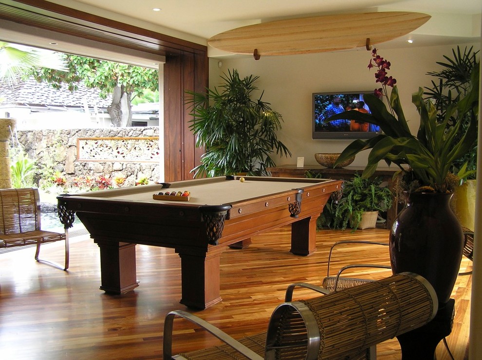 Esempio di un grande soggiorno tropicale aperto con sala giochi, pareti beige, pavimento in legno massello medio e TV a parete