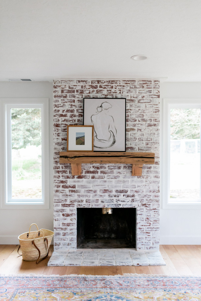 Modelo de sala de estar abierta de estilo de casa de campo de tamaño medio con paredes blancas, suelo de madera clara, todas las chimeneas, marco de chimenea de ladrillo y suelo marrón