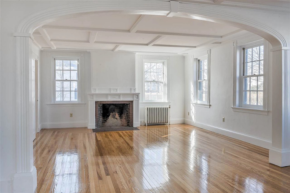 Geräumiges, Offenes Klassisches Wohnzimmer mit grauer Wandfarbe, braunem Holzboden, Kamin, Kaminumrandung aus Holz, braunem Boden und Holzdecke in Boston