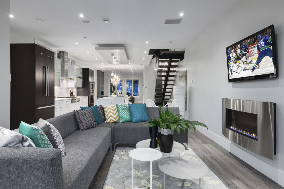 Стильный дизайн: открытая гостиная комната в современном стиле с стандартным камином, фасадом камина из металла и телевизором на стене - последний тренд