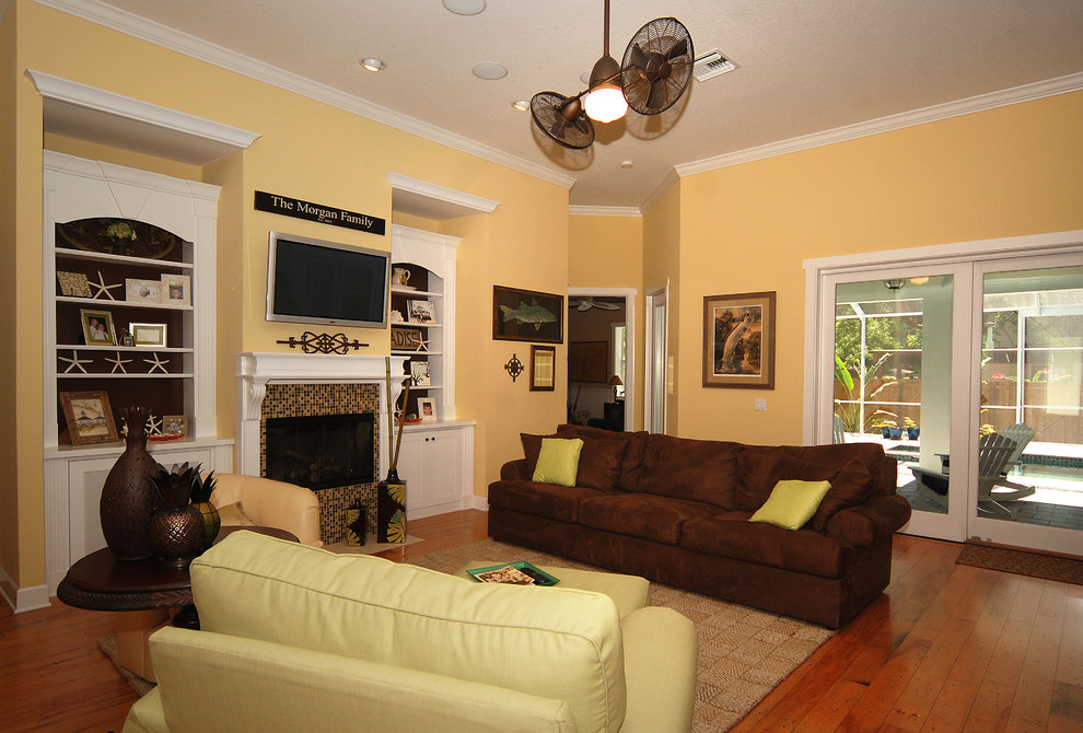 Aménagement d'une salle de séjour exotique de taille moyenne et ouverte avec un mur jaune, un sol en bois brun, une cheminée standard, un manteau de cheminée en carrelage et un téléviseur fixé au mur.