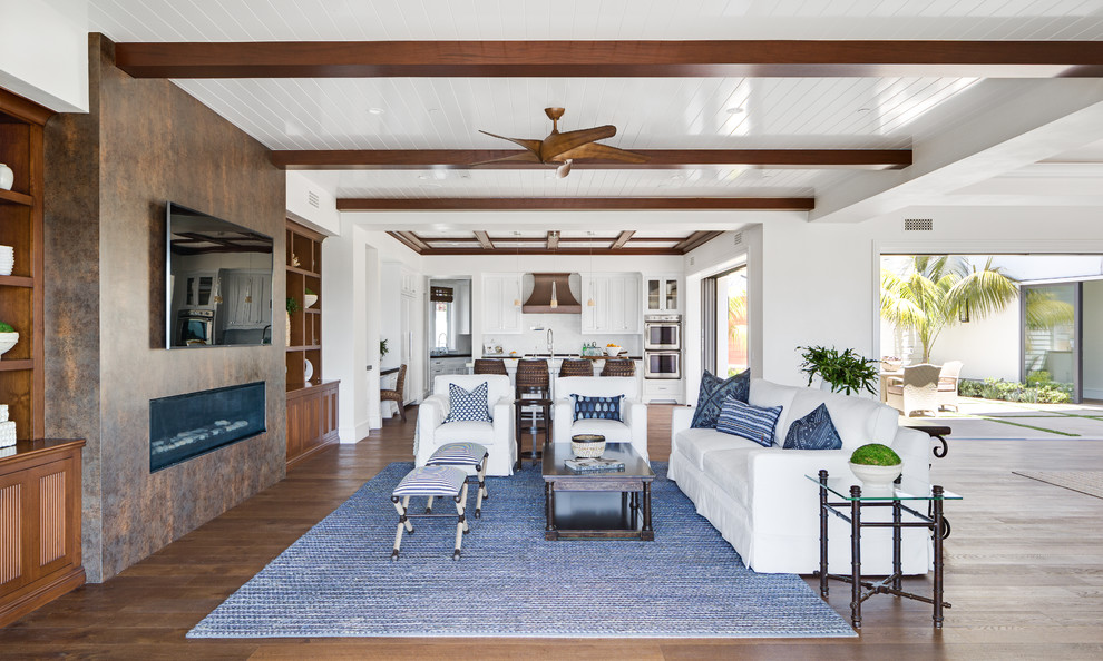 Ejemplo de sala de estar abierta costera con paredes blancas, suelo de madera en tonos medios, chimenea lineal y televisor colgado en la pared